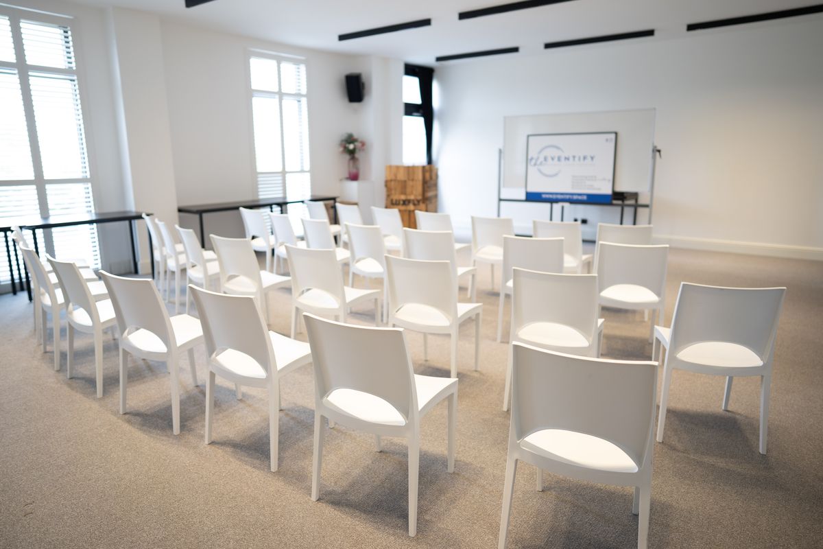 Chaises blanches en rangs face à l'écran, salle lumineuse